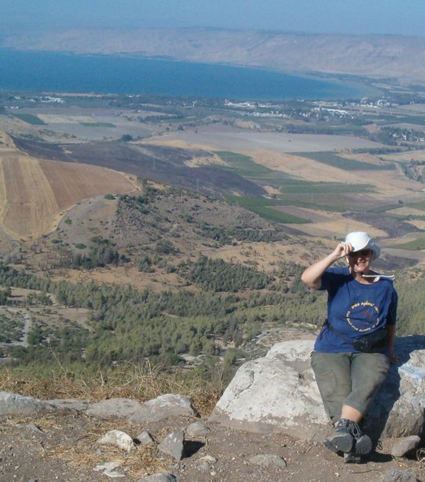 Diana holding her hat from the wind with the Kinneret (Sea of Galilee) and the Golan Heights in the background